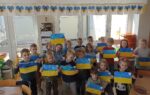 Zdjęcie przedstawia dzieci trzymające kartki z flagą Ukrainy