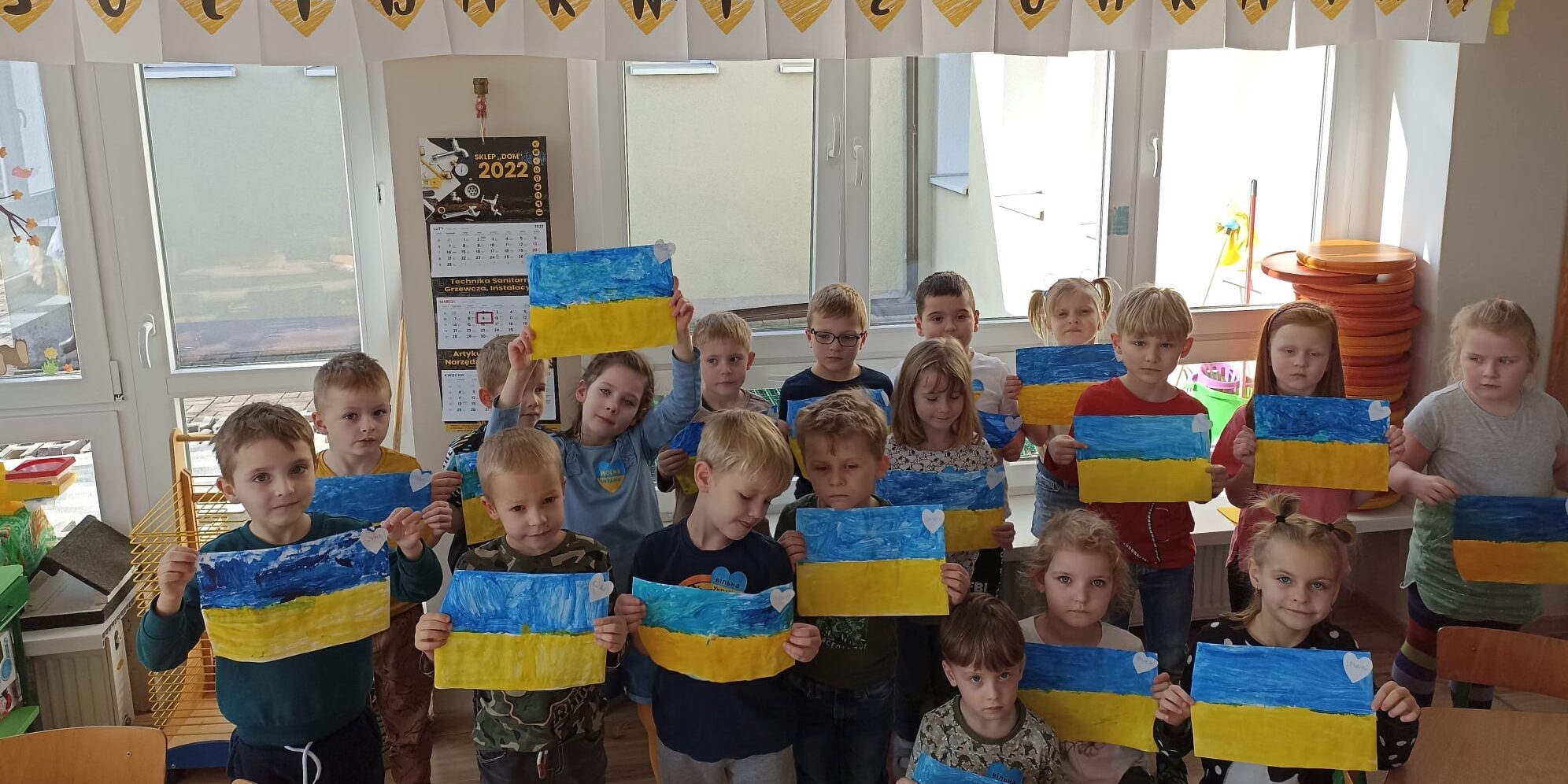Wąbrzeźno. Dzień Ukrainy w Przedszkolu Miejskim Bajka – 13.03.2022r (30) Zdjęcie przedstawia dzieci trzymające kartki z flagą Ukrainy